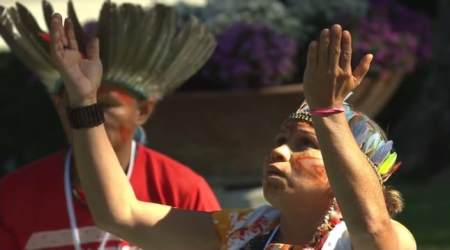 Indigenous woman raises hands in prayer to Pachamama during pagan rite.